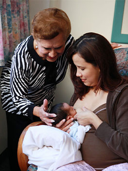 Woman breastfeeding her baby with support from another older woman.
